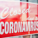 Man hanging a sign on a restaurant door that says, "Closed due to Coronavirus"